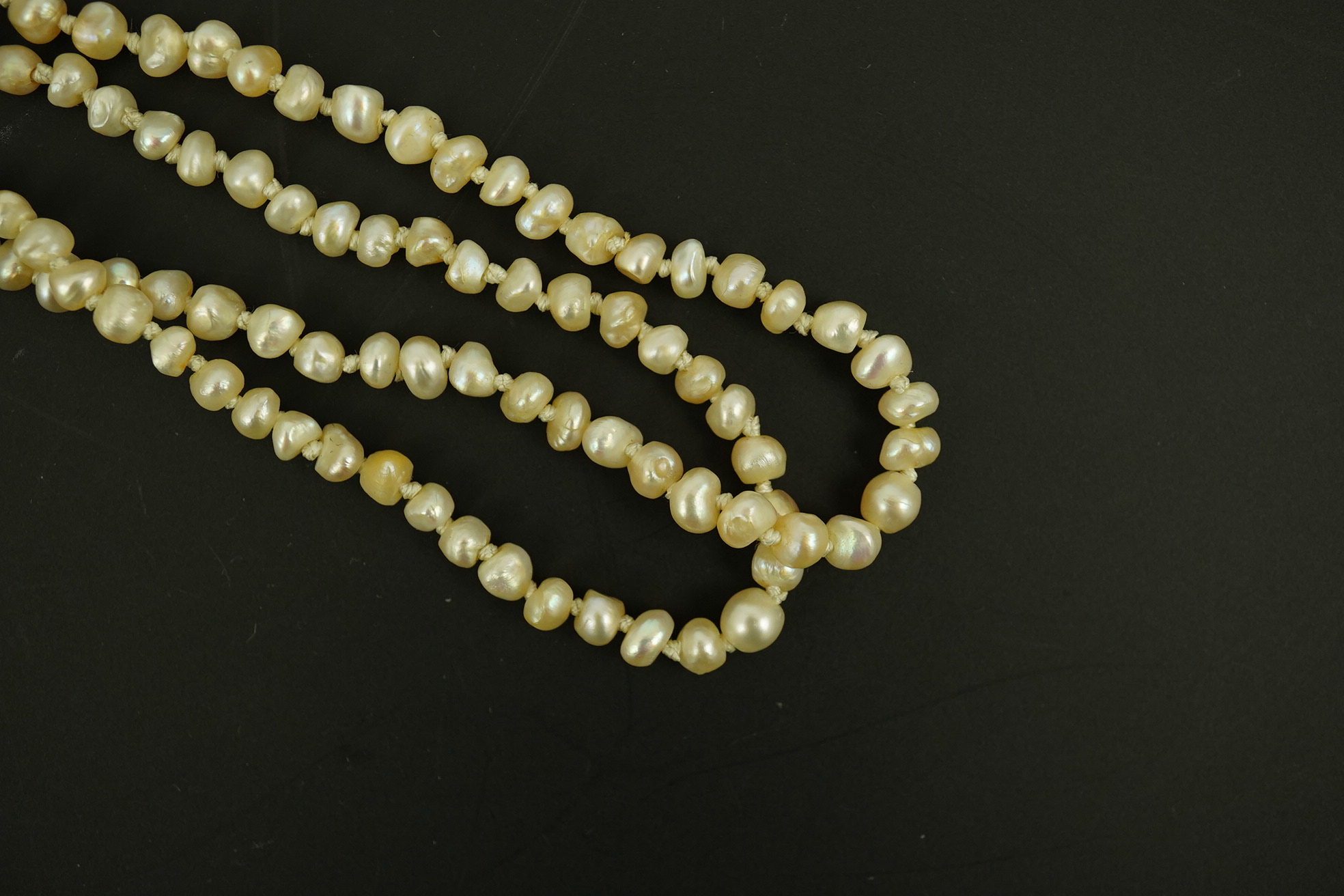 An antique twin strand baroque pearl necklace, with pearl set gold clasp bordered with single chain set with four graduated old mine cut diamonds